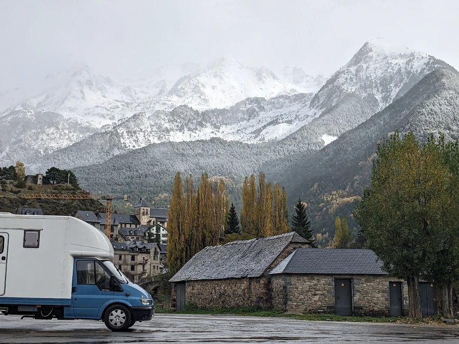 A campervan parked below snow-covered mountains under an overcast sky